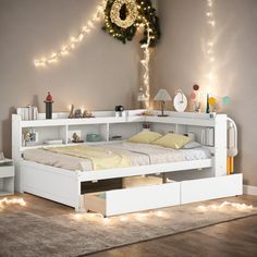 a white bed with drawers underneath it in a room filled with lights and garlands