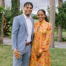 a man and woman standing next to each other in front of some trees on the grass