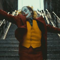 a man dressed as the joker is walking down some stairs with his arms outstretched in triumph