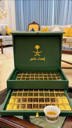 a green box with gold bars in it and a cup on the table next to it