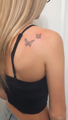 the back of a woman's shoulder with two butterflies tattoo on her left side