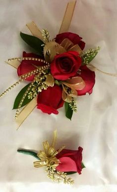 two red roses are sitting on a white sheet and one is holding a gold ribbon