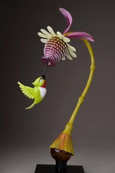 a vase with a flower and a bird on it's head in front of a gray background