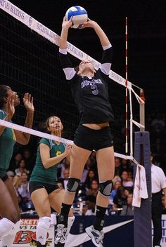 a volleyball player jumps to hit the ball over the net while other players look on