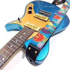 an electric guitar with a blue body and floral design on it's neck, resting against a white background