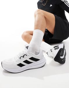 a man sitting on the ground with his feet crossed and wearing adidas shoes in front of him