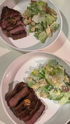 two white plates with steak and salad on them