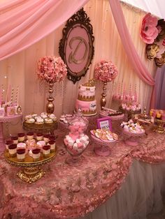 a table topped with cakes and cupcakes under a pink drape covered ceiling