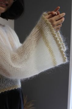 a woman wearing a white sweater and holding up a knitted arm warmer in front of a window