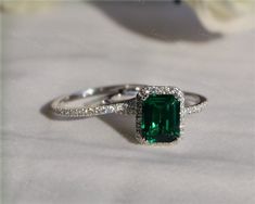 an emerald colored stone surrounded by diamonds on top of a white cloth with flowers in the background