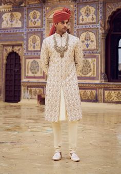 Elevate your look with this light beige raw silk sherwani, exquisitely embroidered with kasab and highlighted with dabka, beadwork, and crystals. Paired with a cotton silk kurta and churidar. Beige Raw Silk Sherwani With Dabka, Unstitched Beige Sherwani With Naqshi Detailing, Beige Sherwani With Resham Embroidery, Traditional Cream Sets With Pearl Embroidery, Traditional Beige Raw Silk Sherwani, Beige Raw Silk Sherwani With Zari Work, Beige Sherwani With Zari Work, Traditional Drape, Unstitched Beige Sherwani With Zari Work, Festive Off-white Raw Silk Sherwani