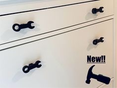 a white dresser with black handles and some stickers on the drawer doors that say new