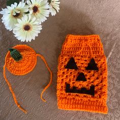 an orange crocheted pumpkin hat and diaper cover next to white daisies