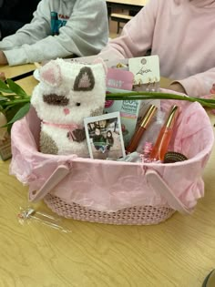 a teddy bear sitting in a pink basket filled with makeup and personal care items on a table