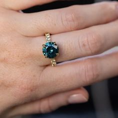 a close up of a person's hand holding a ring with a blue stone