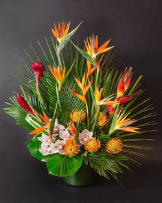 an arrangement of tropical flowers and greenery in a green vase on a black background