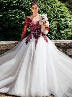 a woman in a white and red wedding dress holding a small dog on her shoulder