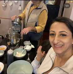 a woman sitting at a table in front of a coffee maker with other people around her