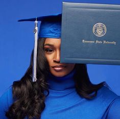 a woman wearing a blue graduation gown and holding up a book to her face with the seal of approval on it