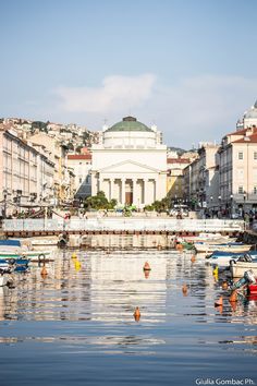 there are many boats that are in the water near some buildings and people walking around