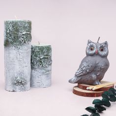 an owl figurine sitting next to two candles on a wooden stand with green leaves