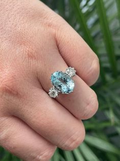 a person's hand holding a ring with an aqua blue stone and diamond accents