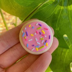 a hand holding a pink frosted donut with sprinkles on it