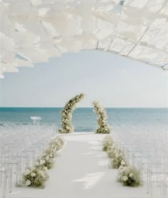 an outdoor ceremony setup with white chairs and flowers on the aisle, overlooking the ocean