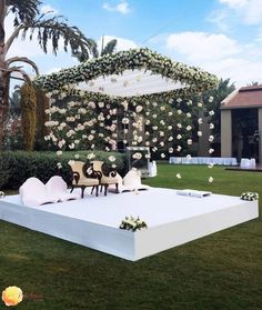 an outdoor wedding setup with white flowers on the stage and chairs set up in front