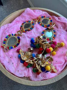 a wooden bowl filled with lots of different colored jewelry on top of a pink cloth