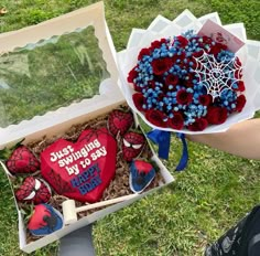 two decorated heart shaped cakes in a box on the grass with someone's hand