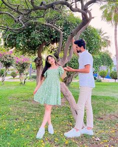 a man standing next to a woman in a green dress under a tree with yellow flowers