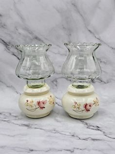 two glass vases sitting next to each other on a marble counter top with flowers painted on them