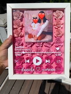 a person holding up a pink and white photo frame with roses on the front, two hearts in the middle