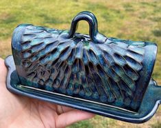 a hand holding a blue ceramic purse on it's side in front of some grass