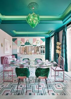 a dining room with pink and green chairs, blue walls, and a glass table