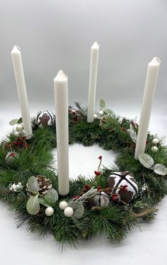 a christmas wreath with candles and decorations on it, sitting in front of a white background