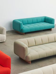 four different colored couches sitting next to each other in a room with concrete flooring