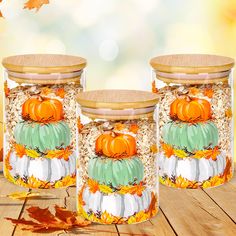 three glass jars with painted pumpkins and leaves on the lids are sitting on a wooden table