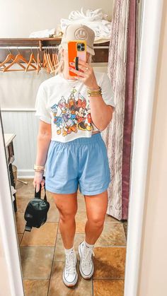 a woman taking a selfie in front of a mirror wearing blue shorts and white sneakers