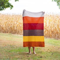 a woman standing in front of a corn field holding a colorful blanket