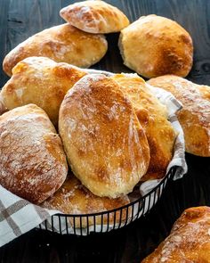 a basket filled with lots of bread on top of a wooden table covered in powdered sugar