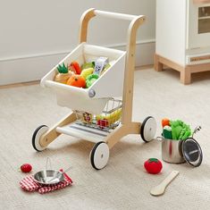 a toy shopping cart with fruits and vegetables in it on the floor next to other toys