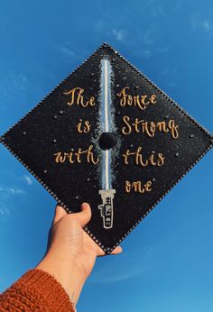 a hand holding a graduation cap that says the force is strong with this one