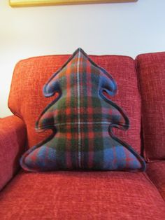 a plaid christmas tree pillow sitting on top of a red couch next to a painting