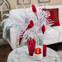 a vase filled with red birds sitting on top of a table next to a white couch