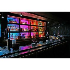 a dimly lit bar with liquor bottles and glasses on the shelves, along with neon lights