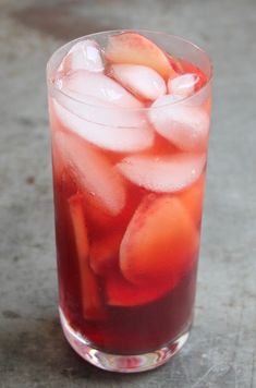 a glass filled with ice and fruit on top of a cement floor next to a table