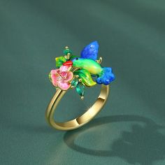 You can wear them stacked together or separately. This beautiful ring have been created from sterling silver with hand painted enamelling, each ring is adorned with a lovebird and flowers. It looks like a hummingbird is hovering over the flower on your ring! Elegant and unique!Carat Weight: 0.24 ctStone Size: 1,1.5,2*4,1.5*3,1 mmStone Type: Jeulia® StoneNumber of Stones: 7 Stone Shape: Round, MarquiseStone Color: Diamond White, Fuchsia, Emerald GreenWeight: 4.71 gWidth: 2.15 mmHeight: 6.75 mmThickness: 1.1 mmMaterial: 925 SilverPlating Color: Yellow Gold Green Enamel Ring For Wedding, Flower-shaped Enamel Ring As Gift, Flower Shaped Enamel Ring As A Gift, Flower-shaped Enamel Ring For Gift, Floral Enamel Ring As Gift, Flower Shaped Enamel Ring For Gift, Green Enamel Wedding Ring, Elegant Hand Painted Enamel Ring Perfect For Gifting, Wedding Green Enamel Ring