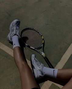 a woman's legs and tennis racket on the ground in front of her